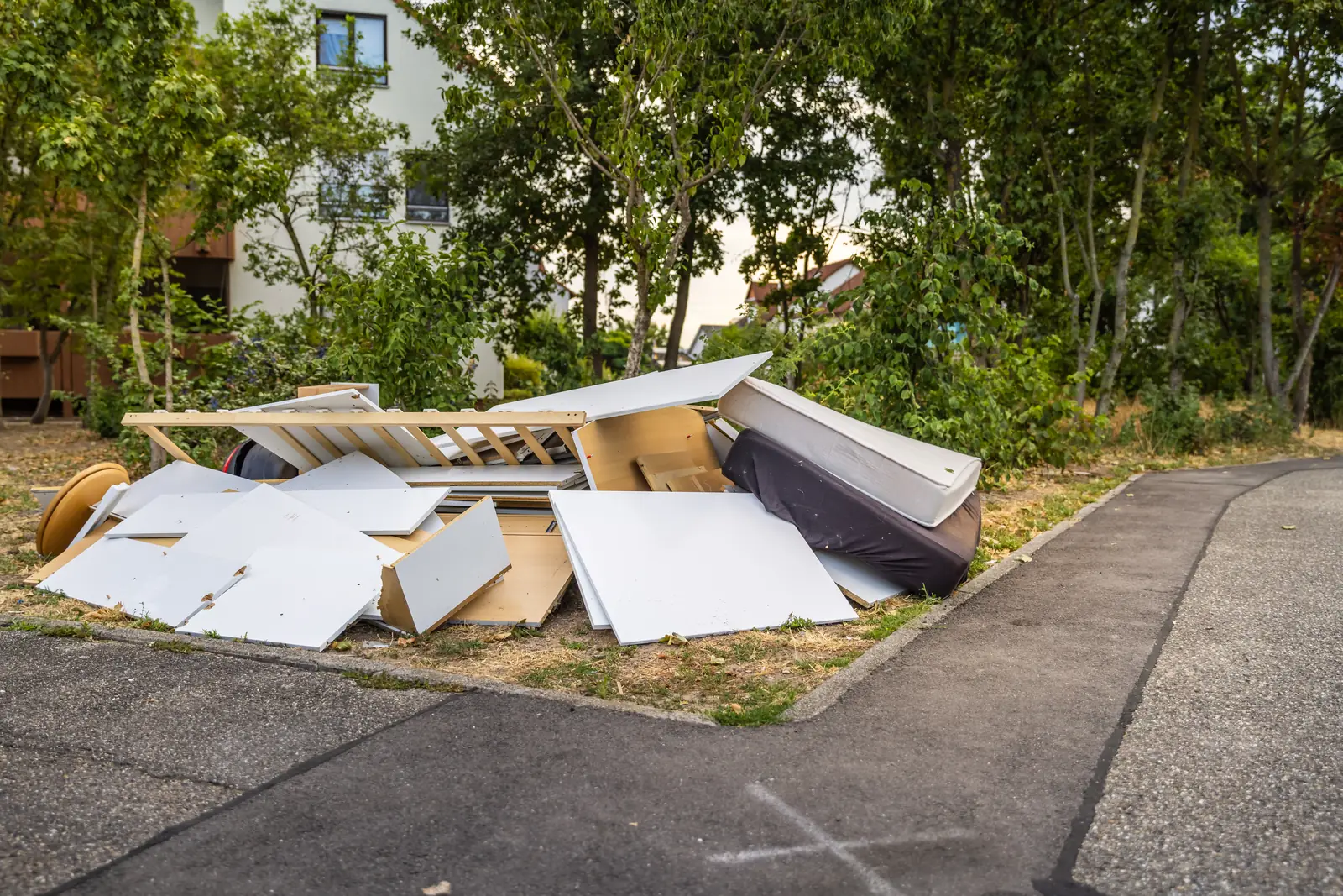 Curbside pile of broken furniture panels, a bed frame and mattresses